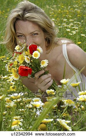 Picture - Woman is sitting in a meadow with a bunch of flowers. Fotosearch