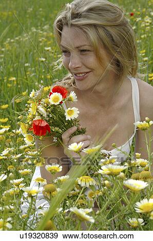 Stock Photo - Woman is sitting in a meadow with a bunch of flowers. Fotosearch