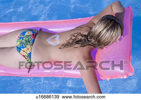 Stock Photo - Woman on a airmattress with a sun lotion heart on her back. Fotosearch