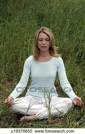 Stock Image - Woman sitting cross legged on meadow. Fotosearch