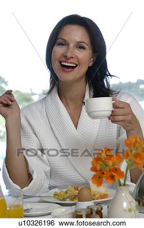 Stock Photograph - Woman wearing a bathrobe is having breakfast. Fotosearch