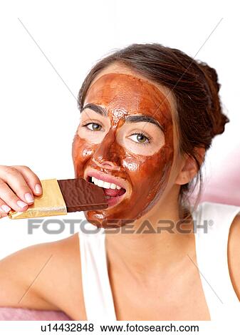 Stock Photo - Woman with face mask eating a candy bar. Fotosearch