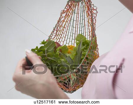 Stock Image - Woman with fruit and vegetables in a string bag. Fotosearch