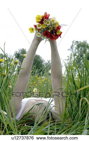 Women is lying in a meadow and holding a bunch of flowers in the air View Large Photo Image Stock Photograph - Women is lying in a meadow and holding a bunch of flowers in the air. Fotosearch