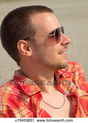 Stock Image - Young man on the beach with sunglasses. Fotosearch