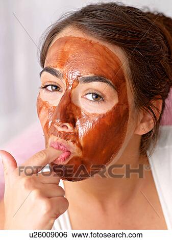 Stock Photograph - Young woman nibbling from chocolate mask. Fotosearch
