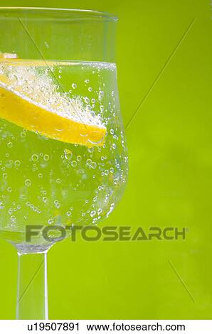 Stock Image - Zitrone in einem Wasserglas mit grünem Hintergrund. Fotosearch