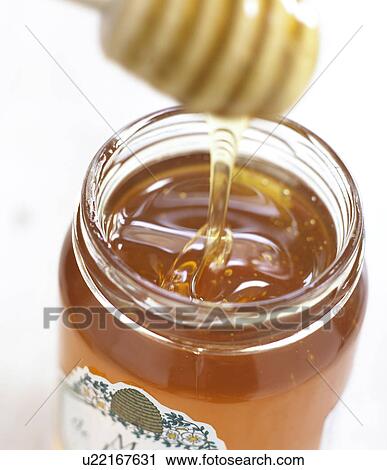 Stock Image - Honey is running from spoon into glass. Fotosearch