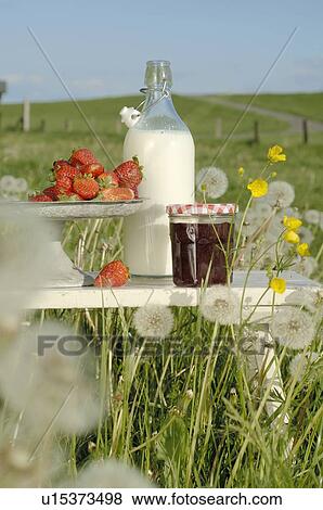 Stock Photo - Jam, a bottle of milk and strawberries on a summer meadow. Fotosearch