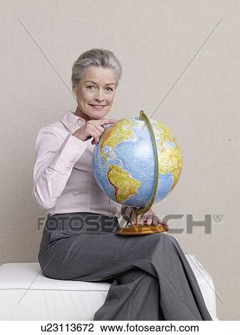 Stock Image - Senior citizen in business wear with a terrestrial globe on her lap. Fotosearch