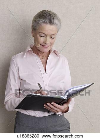 Stock Image - Senior citizen in business wear writing in book. Fotosearch