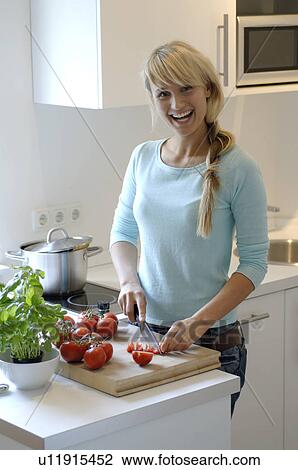 Stock Image - Teenage girl slicing tomatoes in kitchen. Fotosearch