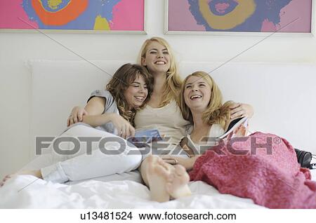 Three sisters reading magazines in bed and laughing View Large Photo Image Picture - Three sisters reading magazines in bed and laughing. Fotosearch