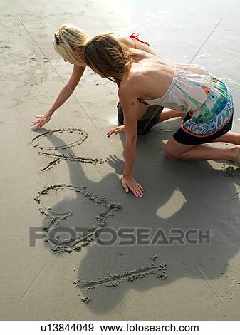 Stock Photo - Two young women writing in the sand. Fotosearch