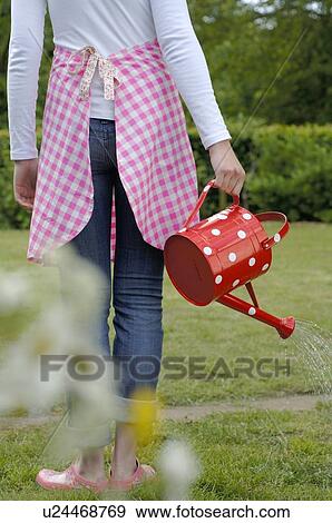 Stock Photo - Woman in garden watering flowers. Fotosearch