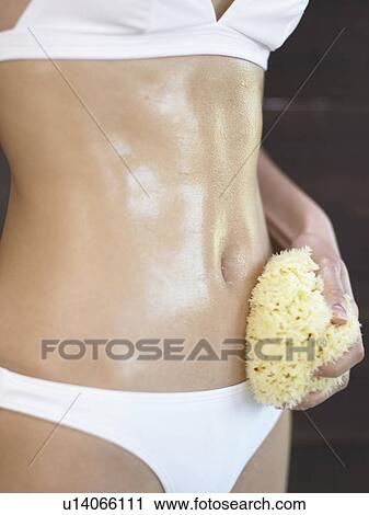 Stock Image - Woman oiling her body with sponge. Fotosearch