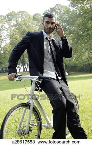 Young business man leaning on a bicycle and using a mobile View Large Photo Image Stock Image - Young business man leaning on a bicycle and using a mobile. Fotosearch