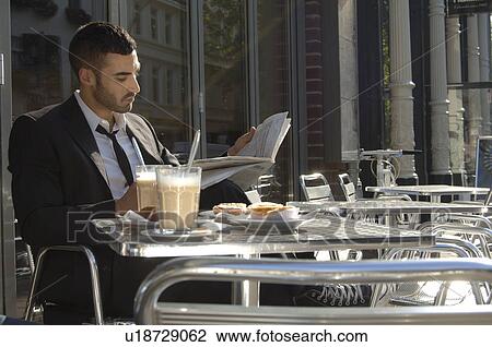 Stock Image - Young business man relaxing in cafe and reading newspaper. Fotosearch