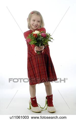 Stock Image - Young girl wearing large shoes and holding bunch of flowers. Fotosearch