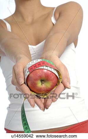 Stock Image - Young woman holding apple with measuring tape. Fotosearch