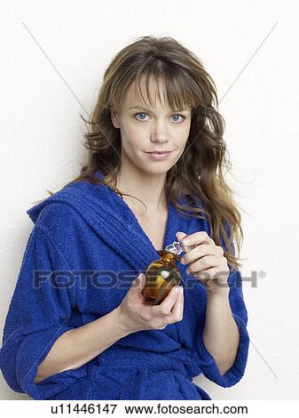 Stock Photo - Young woman in blue bath robe holding glass bottle. Fotosearch