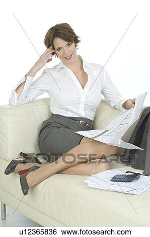 Stock Photograph - Young woman in business dress working on sofa. Fotosearch