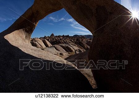 Stock Image - Arch formation of sandstone, against blue early morning sky, with sunstar fromation, Alabama hills, with range beyond. Fotosearch