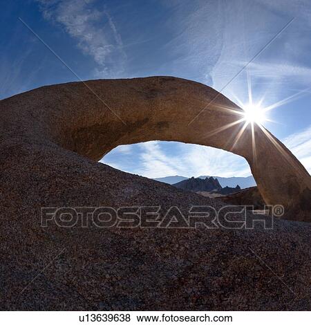 Stock Photo - Arch formation of sandstone, against blue early morning sky, with sunstar fromation, Alabama hills, with range beyond. Fotosearch