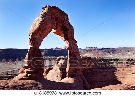 Stock Photo - Delicate Arch in early morning sunlight against blue sky, mountain range beyond, Arches, Utah. Fotosearch