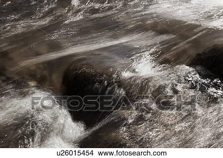 Picture - Desaturated image of river flowing over rocks, motion slowed to capture linear highlights, and texture of water, Utah. Fotosearch