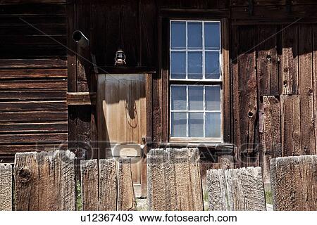 Stock Image - Detail of wooden house with doorway, window overlooking garden and wooden picket fence, desaturated image, Bodie pioneer village, California. Fotosearch