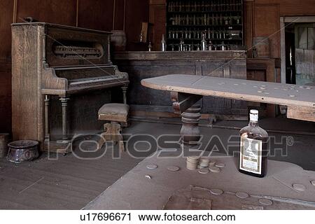 Stock Image - Drinking saloon as seen from inside with piano, gaming tables and beer bottles behind bar, desaturated image, Bodie pioneer village, California. Fotosearch