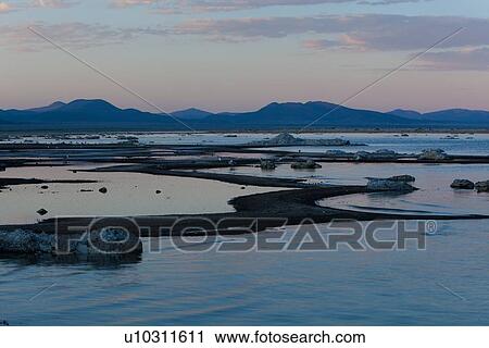 Stock Image - Mono Lake tufas and shoreline in curving pattern, with pink skies and purple mountain range reflections in calm waters at sunset. Fotosearch