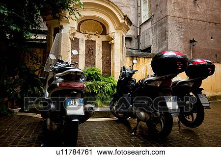 Stock Image - Motorbikes parked near Baroque fountain, cobblestone street, Rome. Fotosearch