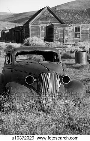 Old car abandoned in field, front side view, with wooden house and hills beyond, desaturated image, Bodie pioneer village, California View Large Photo Image Stock Photo - Old car abandoned in field, front side view, with wooden house and hills beyond, desaturated image, Bodie pioneer village, California. Fotosearch