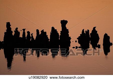 Stock Image - Orange dawn light silhouettes the tufa formations of Mono Lake on a calm summer morning, with deep reflections in the still water. Fotosearch