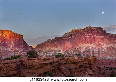 Stock Image - Panorama at Panorama Point, Utah, sunset light on red mountain rock, pink-grey cloud in blue sky, with full moon rising,. Fotosearch