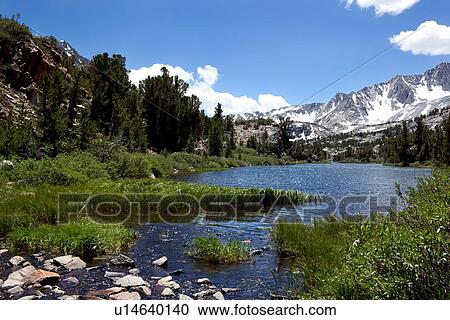 Stock Image - Panorama of clear blue lake against snow-tipped Sierra Nevada mountain range, on sunny summer morning. Fotosearch