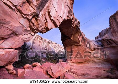 Stock Photo - Panorama of Hickman Bridge, Utah, in early dawn light, pink rock against blue sky and pink clouds, with distant mountains seen through arch. Fotosearch