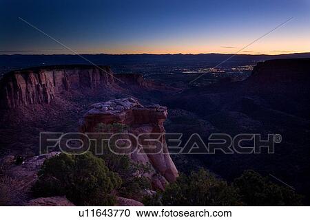 Stock Image - Panorama view of Colorado Monument Valley at dawn, with indigo sky, orange horizon, lights of Grand Junction in distance, Colorado. Fotosearch