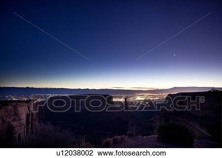 Stock Image - Panorama view of Colorado Monument Valley at dawn, with starlit sky, lights of Grand Junction in distance, Colorado. Fotosearch