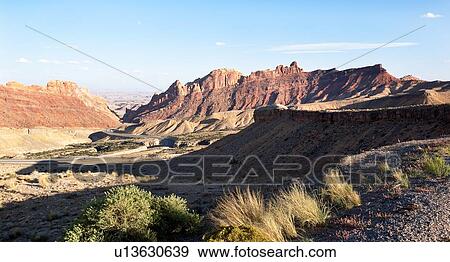 Stock Photo - Panorama view of mountains and interstate highway winding through gorge, San Rafael Reef, at sunset with blue sky and puffy clouds, Utah. Fotosearch
