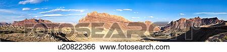 Stock Photograph - Panorama view of mountains and interstate highway winding through gorge, San Rafael Reef, at sunset with blue sky and puffy clouds, Utah. Fotosearch