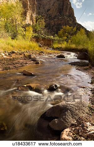 Stock Photo - Pleasant Valley, river with aspens alongside, steep rocky slope to mountains, blue sky, white puffy clouds, water motion slowed over rocks, Utah. Fotosearch