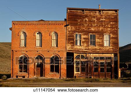 Picture - Red brick, and wooden buildngs on main street, facades lit in dawn light, with blue sky, Bodie pioneer village, California. Fotosearch