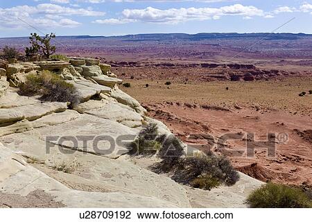 Stock Image - Rocky overlook with valley, distant mountains, blue sky with fluffy white clouds, fall morning, Utah. Fotosearch