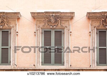 Stock Photograph - Rome street, window detail of house, with pink stucco walls, pale green shutters, sculptured head and garlands decorating. Fotosearch