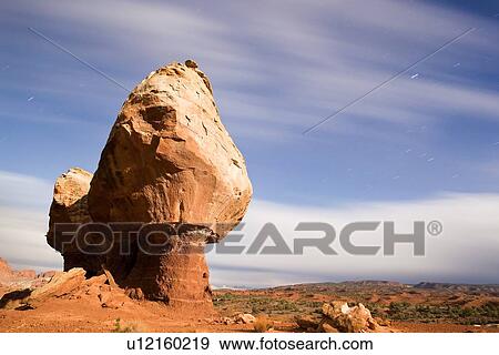 Stock Photo - Single butte - red rock formation- against blue night sky, with cloud movement and star trails, mountain range beyond, Utah. Fotosearch