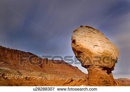 Stock Photo - Single butte - red rock formation- against blue night sky, with cloud movement and star trails, mountain range beyond, Utah. Fotosearch