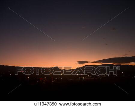 Stock Image - View of Grand Junction malls and roads with night lights illuminated, mountain skyline and pink glow of dawn in indigo sky, Colorado. Fotosearch